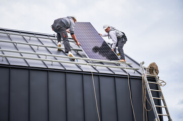 Builders installing solar panel system on roof of house. Men workers in helmets carrying...