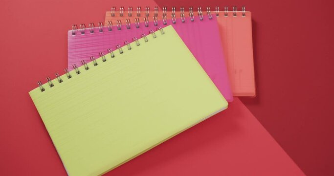 Overhead view of colourful notebooks on red background, in slow motion
