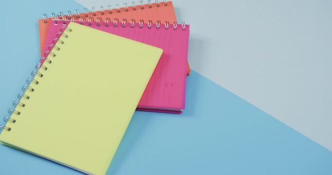 Overhead view of colourful notebooks on blue background, in slow motion