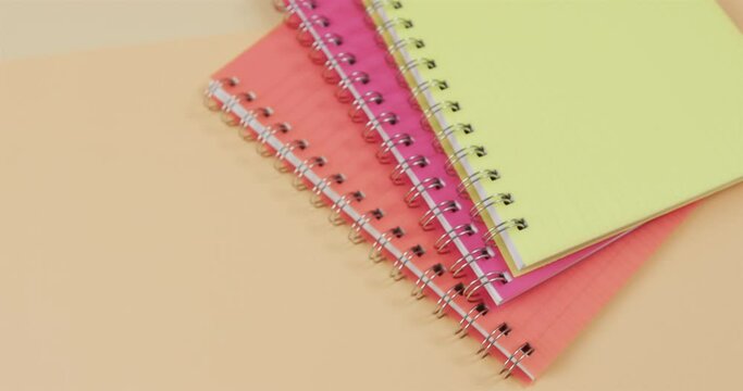 Overhead view of colourful notebooks on beige background, in slow motion