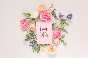 Overhead view of roses, chrysanthemums and alstroemeria flowers arranged around a Valentine's Day card with the words Love you forever