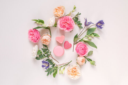 Overhead view of a Floral arrangement of roses, chrysanthemums, alstroemeria  flowers and foliage around heart shape candies on a pink background