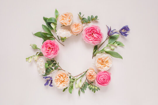 Overhead view of a circular Floral arrangement of roses, chrysanthemums, alstroemeria flowers and foliage on a pink background