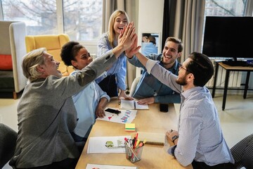 Successful business people giving each other a high five in a meeting. Two young business professionals celebrating teamwork in an office