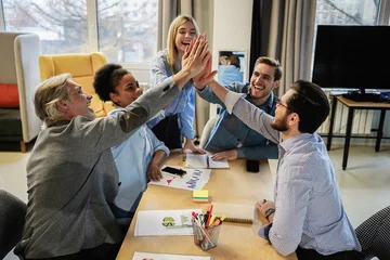 Fotobehang Successful business people giving each other a high five in a meeting. Two young business professionals celebrating teamwork in an office © opolja