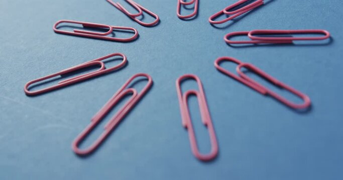 Close up of pink paper clips arranged on blue background, in slow motion