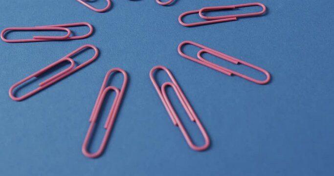 Close up of pink paper clips arranged on blue background, in slow motion
