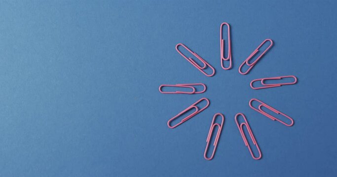 Overhead view of pink paper clips arranged with copy space on blue background, in slow motion