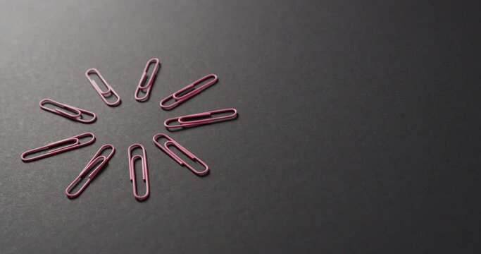 Close up of pink paper clips arranged with copy space on black background, in slow motion
