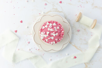 Pink glazed cupcake on retro plate with heart shape sprinkles on white golden marble table background.