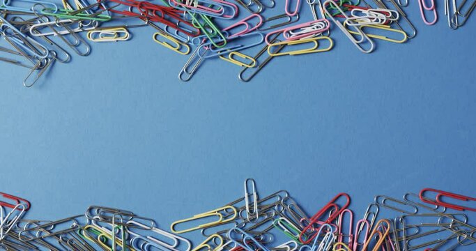 Overhead view of scattered colourful paper clips with copy space on blue background, in slow motion