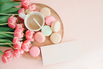 Bouquet of pink tulips, cup of coffee and macaroons on pink background. Anniversary celebration concept. Copy space. Top view