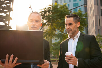 Two trusted business colleagues dressed in formal attire with a computer in hand observing the...