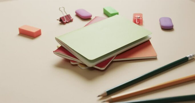 Close up of colourful notebooks with school stationery on beige background, in slow motion