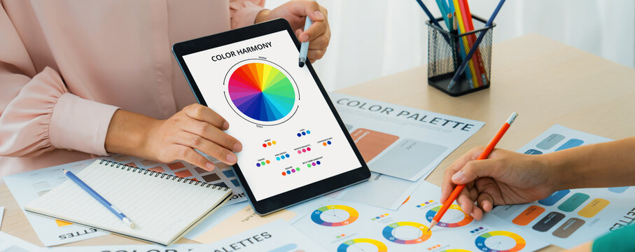 A cropped picture of professional designer selects the color by using color theory and comparing with color wheel on table with designing material and equipment scatter around. Variegated.
