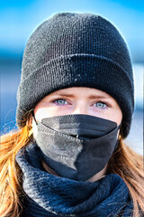 Woman with long red hair and a hat wears an FFP 2 protective mask.