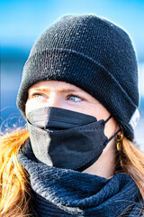 Woman with long red hair and a hat wears an FFP 2 protective mask.