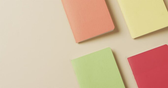 Overhead view of colourful notebooks arranged on beige background, in slow motion
