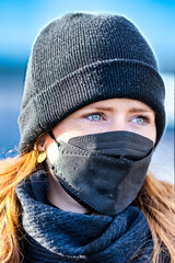 Woman with long red hair and a hat wears an FFP 2 protective mask.