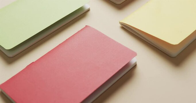 Close up of colourful notebooks arranged on beige background, in slow motion