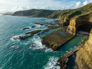 Aerial: Rocky coastline and cove with waves crashing inside it. Murawai, Auckland, New Zealand.,...