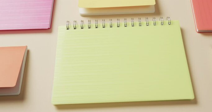 Close up of colourful notebooks arranged on beige background, in slow motion