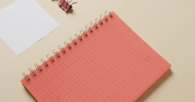 Close up of red notebook and school stationery arranged on beige background, in slow motion