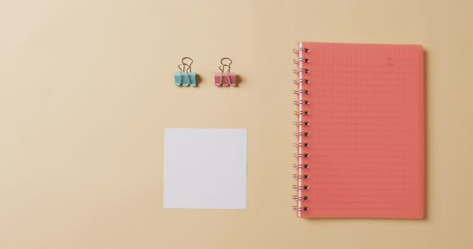 Overhead view of red notebook and school stationery arranged on beige background, in slow motion