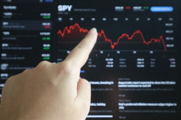 Hand holding digital tablet and pointing at display stock market data with graph and chart for analyze and check before trading stocks online. Red, DIP candles. Investor, trade, finance concept