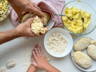The hands of child and father knead the dough for making pies on white table