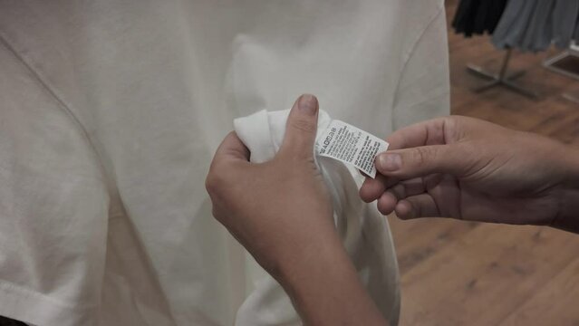 Person checking the label inside a white T-shirt in a clothing store for fabric composition and care instructions