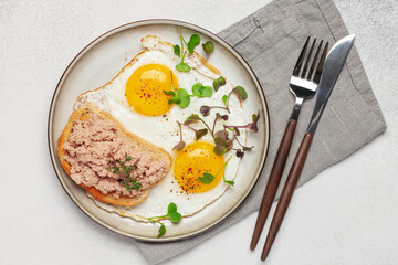 Breakfast - fried eggs and a sandwich with goose pate in a plate on the table. Top view