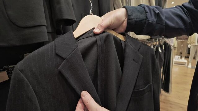 Close-up of a customer's hand selecting a pinstripe suit from a clothing rack in a modern men's fashion store