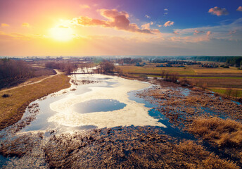 Aerial view of the countryside and frozen winding brook in the evening at sunset light. Beautiful natural landscape with cloudy sky