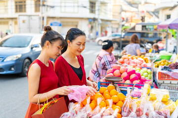 Happy Asian family celebration Chinese Lunar New Year festival together. Mother and daughter choosing and buying fresh fruit orange for celebrating Chinese New Year at Chinatown street market.