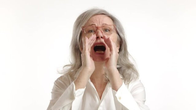 Elderly woman loudly shouting or calling out with hands cupped around her mouth, a gesture of trying to amplify her voice over a distance, isolated on a white background. Camera 8K RAW. 