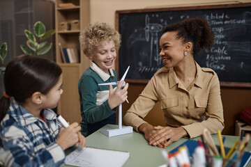Obraz premium Side view portrait of cheerful young teacher explaining eco friendly energy to kids in classroom