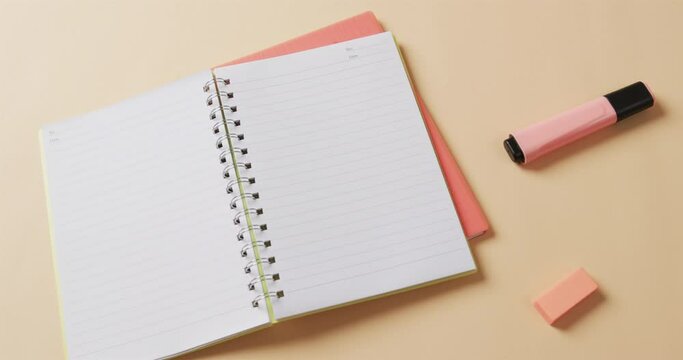 Overhead view of open notebook with school stationery on beige background, in slow motion