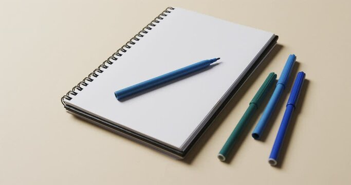 Close up of notebook with blue markers on beige background, in slow motion