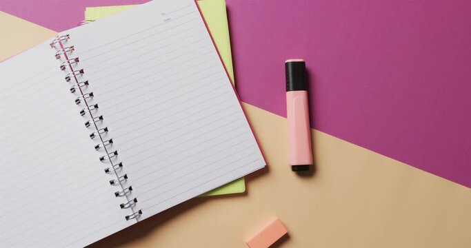 Overhead view of open notebook with school stationery on beige and purple background, in slow motion