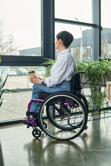 attractive dedicated disabled woman in casual attire in wheelchair holding coffee while in office