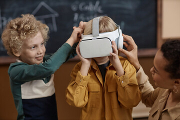 Waist up portrait of schoolboy putting on VR headset for immersive learning experience with teacher helping