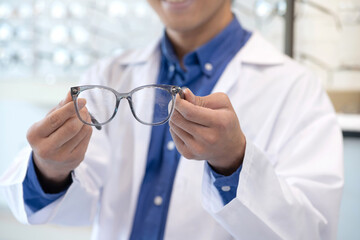 Male optometrist or optician wearing lap coat checking eyeglasses details in a shop, selective focus