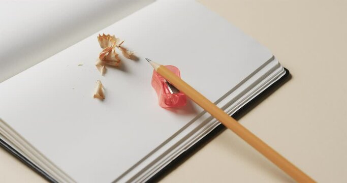 Close up of open notebook with pencil and pencil sharpener on beige background, in slow motion