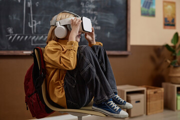 Full length side view of young blond boy wearing VR headset in class and enjoying high tech immersive learning experience