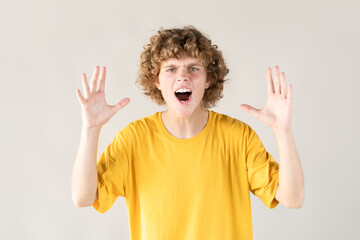 Curly-haired young man in distress and frustration is shown with his hands raised, screaming in...