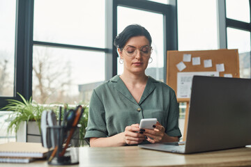 disabled beautiful businesswoman with glasses in casual attire looking at her phone while in office