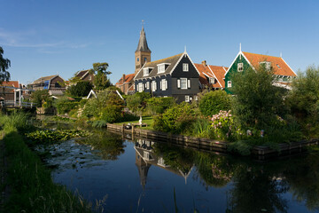 Fototapeta na wymiar MARKEN, NETHERLANDS - JULY 10, 2023: View of the beautiful and typical fishing village of Marken in Netherlands at sunset reflected on a canal.