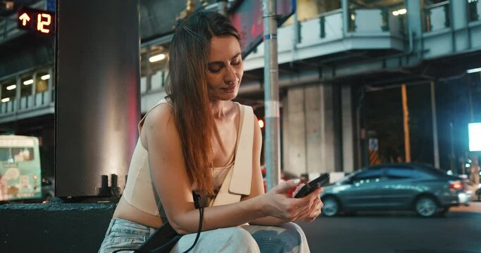 Woman sitting on Bangkok sidewalk calling and waiting for taxi automobiles zooming past. Taxi call facet of modern city life Taxi call easing road commutes Integral part of urban transportation.