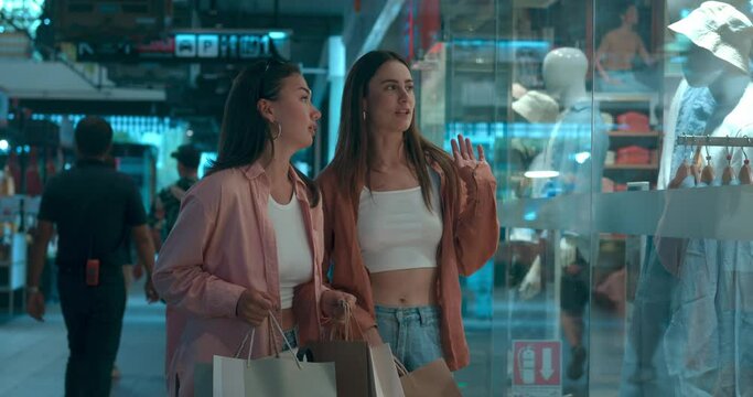 In mall women gaze at showcases contemplating choices Showcases reveal world of shopping happiness. Showcases catalyst for cheerful spending finding new attire Celebrating joy of companionship.